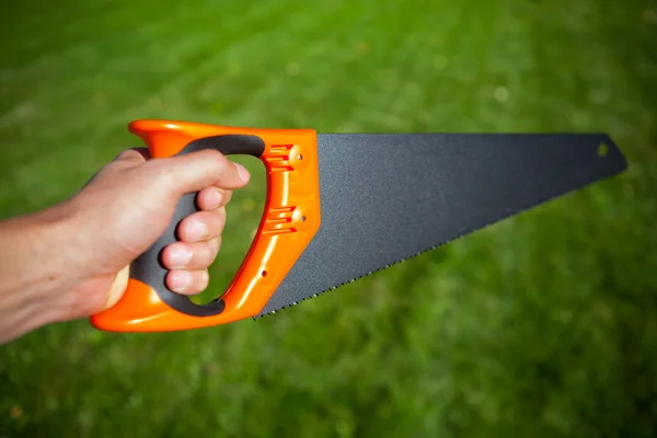 Hand saw against green grass background — Stock Photo, Image