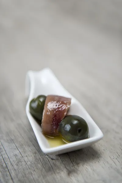 Anchova e azeitonas em uma colher de porcelana — Fotografia de Stock