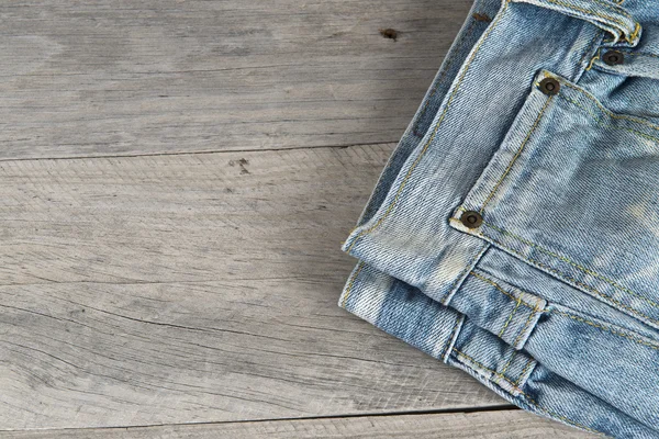 Old worn jeans over a wooden background — Stock Photo, Image