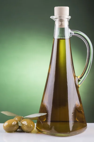 Olive oil bottle and olives on green background — Stock Photo, Image