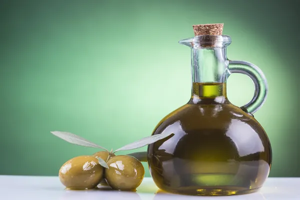 Пляшка оливкової олії та оливки на зеленому фоні — стокове фото