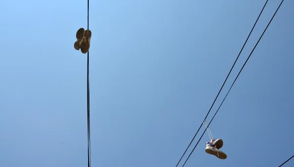 Sneakers opknoping van elektrische draad tegen een blauwe hemel — Stockfoto