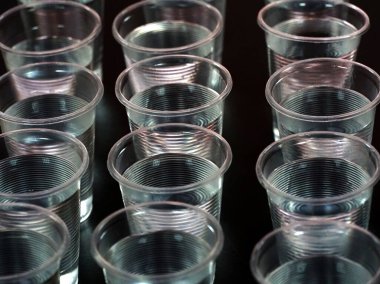 Siyah masa arkasında suyla dolu tek kullanımlık plastik bardaklar..