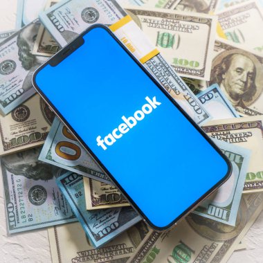 Berlin, Almanya - 2 Şubat 2022: iPhone 12 Pro Max FACEBOOK META şirket logosu ABD dolarları üzerine yerleştirildi