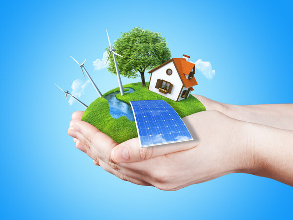 Hands holding clear green meadow with sun battery block, wind mill turbines and countryside house