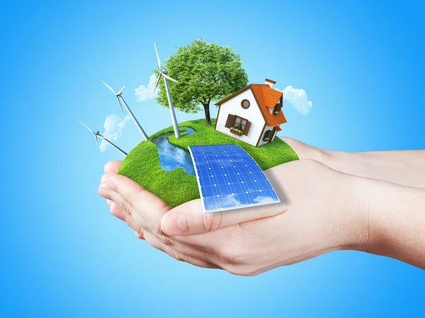 Tartó kezek világos zöld rét naptej akkumulátor, malom szélturbinák és vidéki ház — Stock Fotó