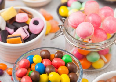 Kavanozda pembe lolipop şekerlemeleri, beyaz masa arkasında çeşitli sütlü çikolatalar ve meyan kökü çeşitleri. 