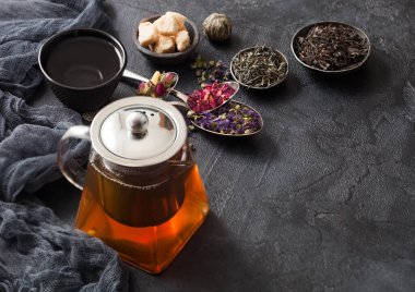 Cam çaydanlık, kaşıklar ve çeşitli çaydanlıklar. Gül tomurcukları, mavi mallow çiçekleri, yeşil ve siyah gevşek çay