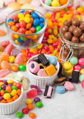 Sütlü çikolatalı şekerler kavanozda çeşitli jöleli diş etleri beyaz masada her çeşit meyan kökü ve farklı ekşi şeker sakızlı çilekli şekerler..