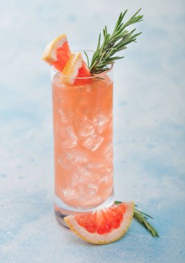 Kırmızı greyfurtlu kokteyl ve viski bardağında votka. Meyve dilimi ve mavi masa arkasında biberiye..