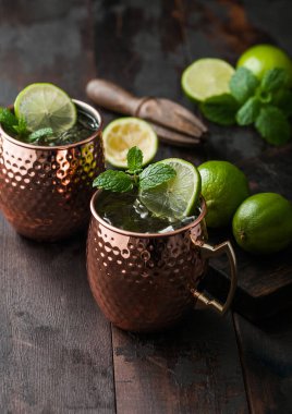 Bakır bardakta Moskova katırı kokteyli, kireç, nane ve ahşap sıkacağı koyu ahşap masa arkasında.. 