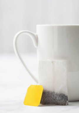 Beyaz arka planda porselen fincanın yanında sarı siyah çay etiketli çay poşeti.. 
