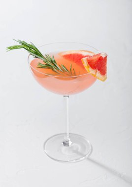 Kristal martini bardağında kırmızı greyfurt yaz kokteyli. Meyve dilimi ve beyaz arka planda biberiye.
