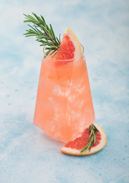 Cocktail with red grapefruit and vodka gin in modern luxury highball glass with fruit slice and rosemary on blue table background.