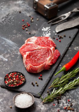 Taş tahtada çiğ pirzola fileto çatal ve bıçakla, tuz ve biberiyeyle siyah mutfak masasının arkasında..
