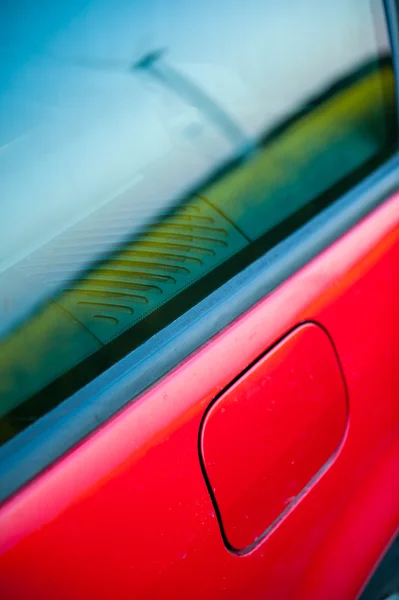 Coche rojo se encuentra al lado del campo donde las flores de violación. y en la distancia se pueden ver los aerogeneradores —  Fotos de Stock