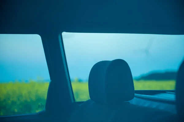 Auto rossa si trova accanto al campo dove fiori di colza. e in lontananza si possono vedere le turbine eoliche — Foto Stock