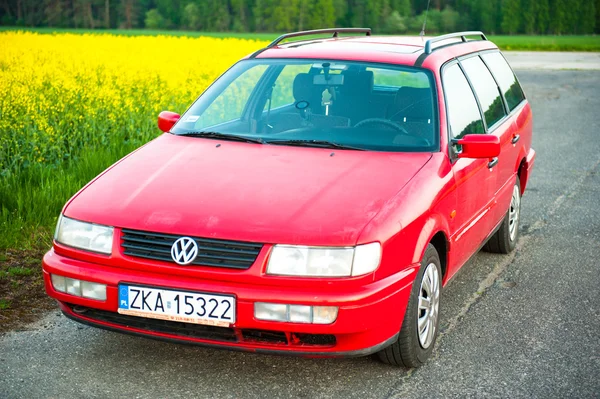 Red car stands next to the field where rape flowers. and in the distance you can see the wind turbines — Stock Photo, Image