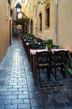 Yunanistan 'ın Girit adasındaki Chania şehrinin dar bir caddesinde restoran sandalyeleri ve masaları kuruldu