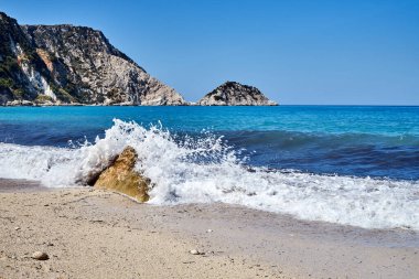 foaming waves, and boulders on a pebble beach of Petani Bay on the island of Kefalonia in Greece