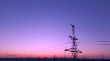 Growing power lines towers against sunset sky