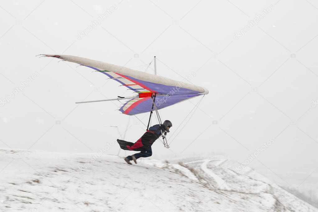 Hang glider pilots runs on the slope in winter. Extreme sport