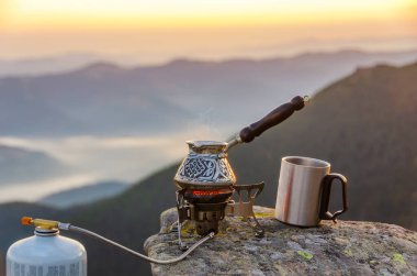 Dağın tepesinde kahve. Harika bir dağ manzarası olan bir taşın üzerinde kahve demliği kaynatıyorum..