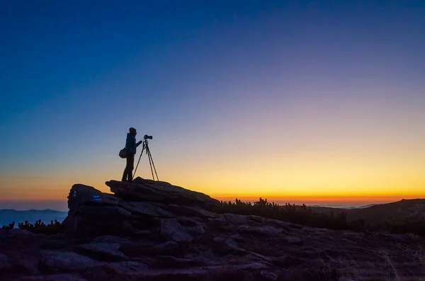 Photographer silhouette on the sunset. Photographer with the tripod takes photos high in the mountains