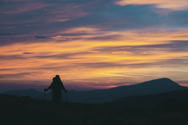 Dağların zirvesinde yürüyüş direkleri olan yürüyüşçü manzaranın tadını çıkar..