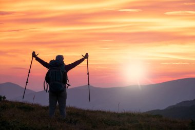 Dağın tepesindeki yürüyüşçü kollarını kaldırarak güneşin doğuşunu kutluyor.