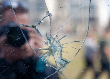 Kameralı adam kırık aynanın önünde duruyor.