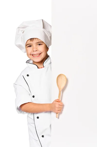 Girl chef with large spoon peeking behind empty board — Stock Photo, Image