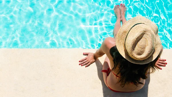 Mulher sentada em uma piscina com chapéu de sol — Fotografia de Stock