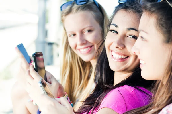 Три девушки общаются со своими смартфонами — стоковое фото