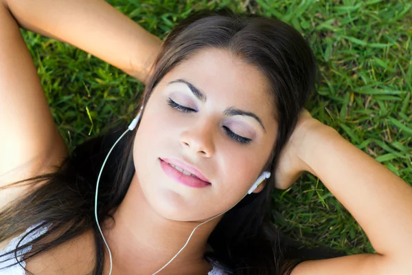 Vrouw luisteren naar muziek liggen op gras — Stockfoto