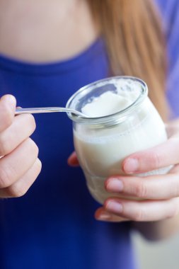 Young woman at home eating yogurt clipart