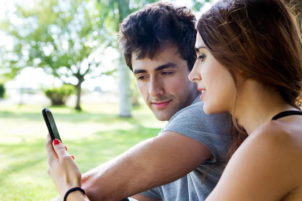 Heureux jeune couple avec smartphone au parc — Photo