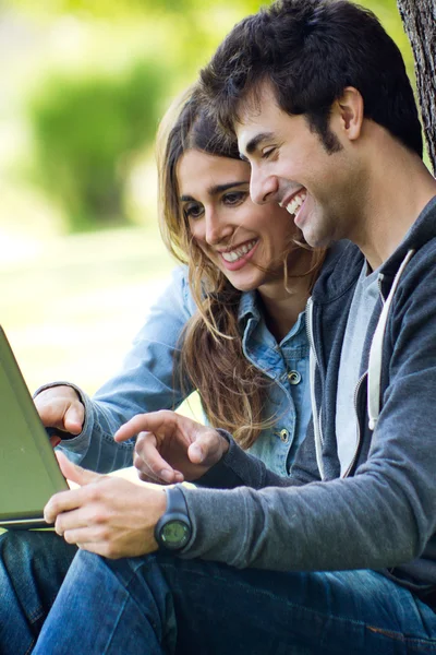 Porträtt av unga par på parken med hjälp av en bärbar dator — Stockfoto