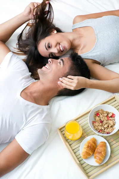 Glückliches junges Paar mit Frühstück auf dem Bett liegend — Stockfoto