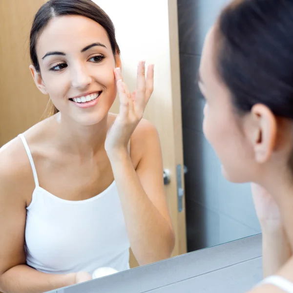 Portrait of young woman applying moisturizer cream on her pretty — Stock Photo, Image