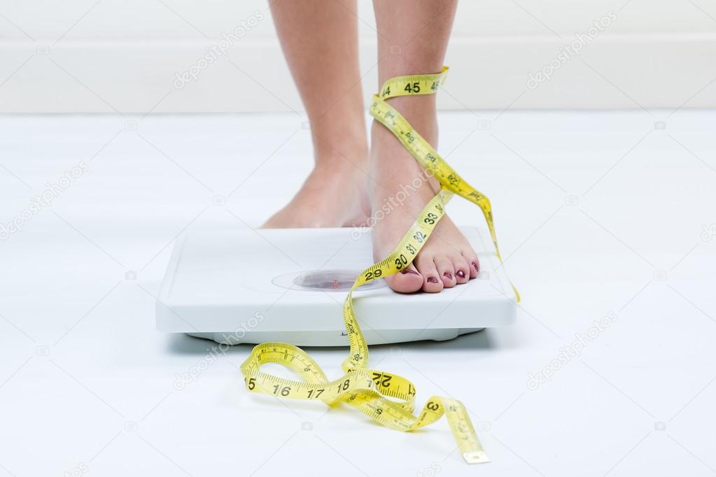 Female feet standing on a bathroom scales and a tape measure
