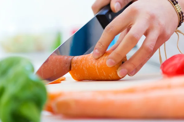 Woman hand cutting carrots in kitchen — Stock Photo, Image