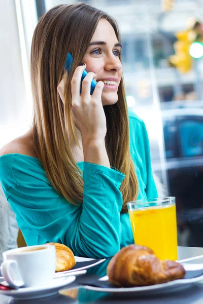 カフェでかわいいブルネットの女性が携帯電話で話しています。 — ストック写真