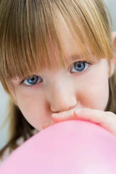 Menina bonito inflando um balão rosa na cozinha — Fotografia de Stock