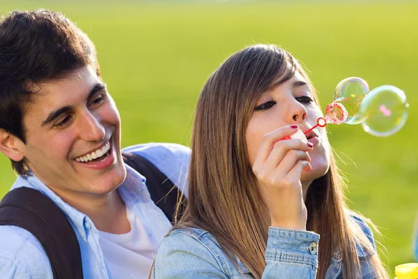 Young couple having fun with soap bubbles in the park — Stock Photo, Image