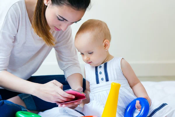 Mother and baby girl using a smartphone at home — Stock Photo, Image