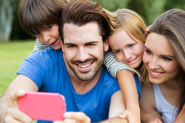 Jovem família feliz tirando selfies com seu smartphone no par — Fotografia de Stock