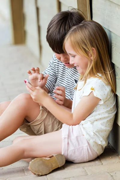 Hhappy hermanitos con smartphone en el parque . — Foto de Stock