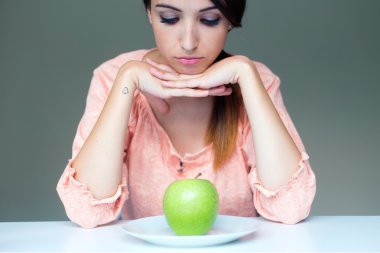 upset brunette woman with green apple on a plate clipart