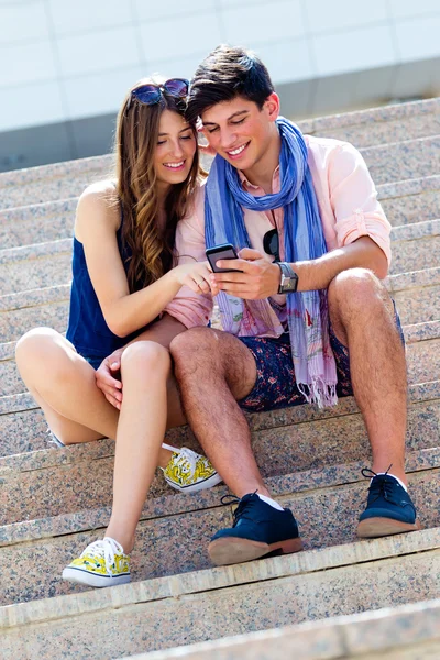 Pareja joven divirtiéndose con teléfonos inteligentes, al aire libre — Foto de Stock